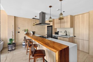 Eine moderne Küche mit einer Holztheke, Barhocker, einem Herd und Pendelleuchten.