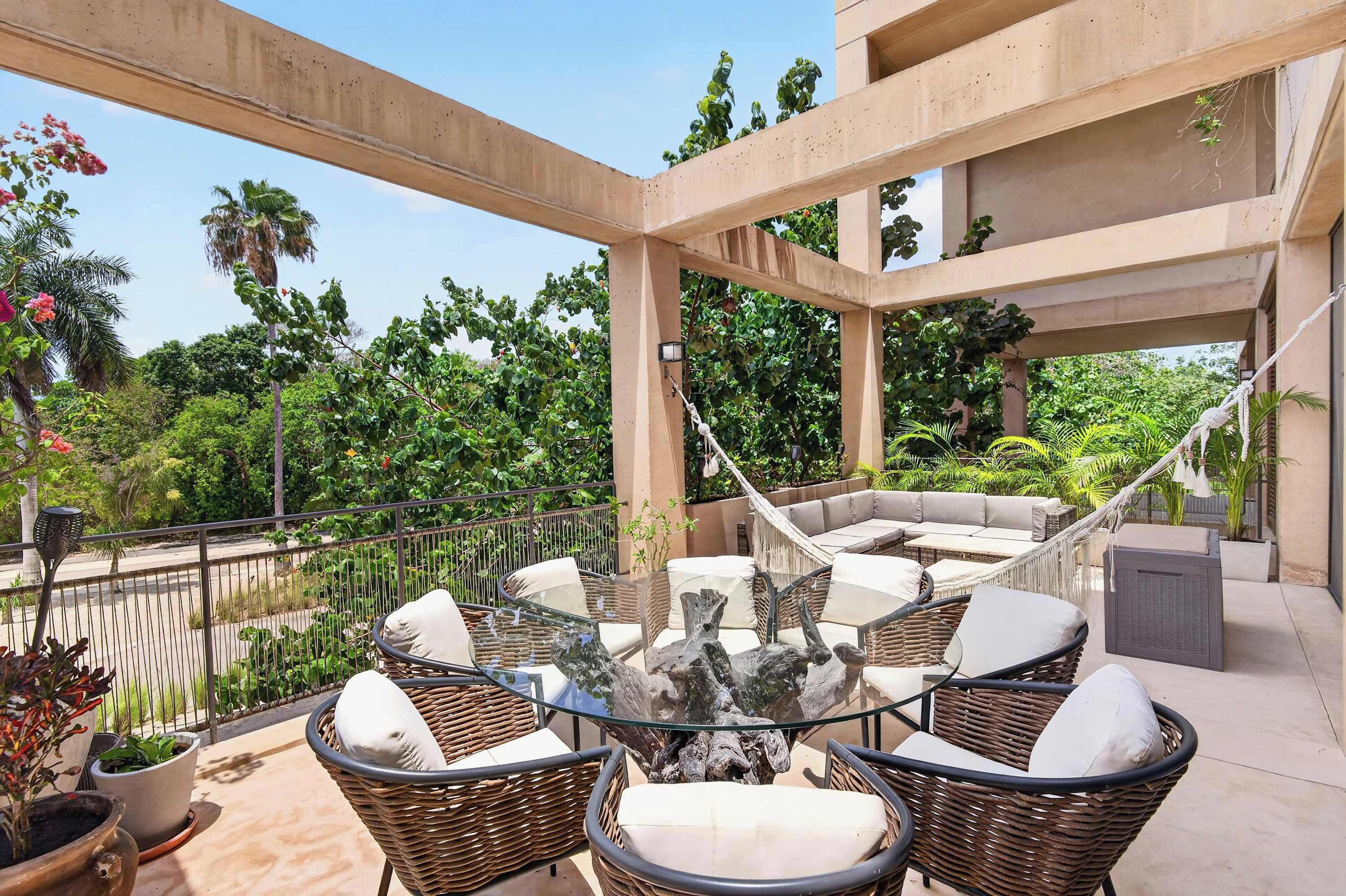 An outdoor patio area with wicker furniture, a glass-top table, and a hammock.