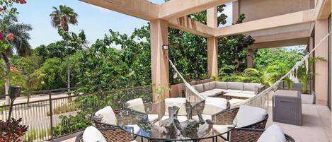 An outdoor patio area with wicker furniture, a glass-top table, and a hammock.