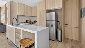 Eine moderne Küche mit Holzschränken, einem Edelstahlkühlschrank, einer Spüle und einem Barhocker.