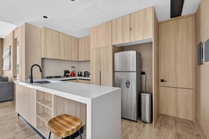Eine moderne Küche mit Holzschränken, einem Edelstahlkühlschrank, einer Spüle und einem Barhocker.