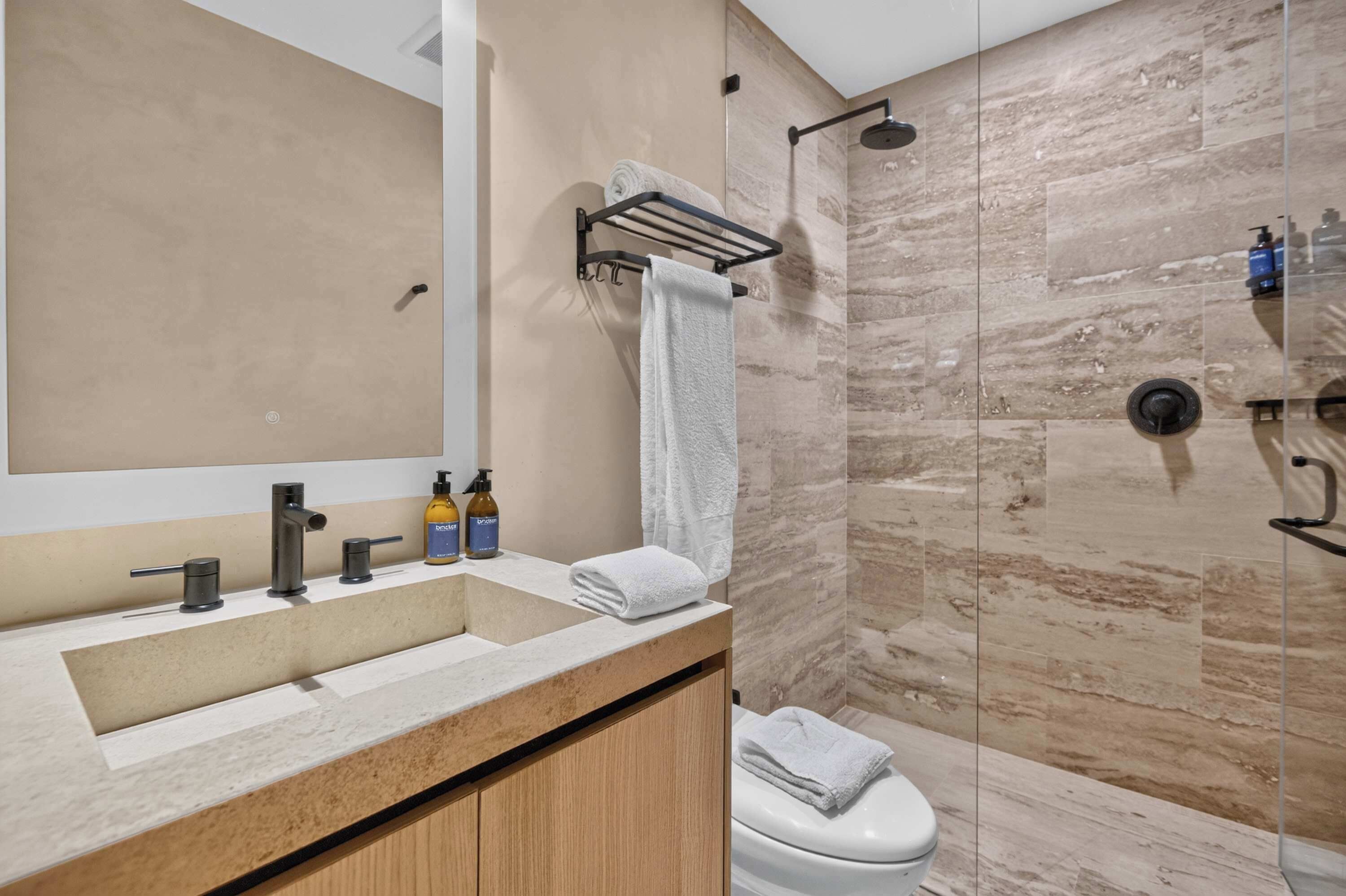 Un baño con tocador de madera, espejo, lavamanos, inodoro y zona de ducha.