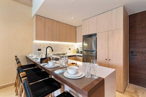 A modern kitchen with a central island, stainless steel appliances, and a dining area with a long table and chairs. - Spacious 2BR with Terrace in The Village (Playa del Carmen)