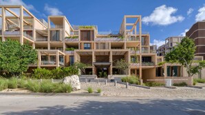 A modern multi-story building with balconies, a central entrance, and surrounding greenery. - Spacious 2BR with Terrace in The Village (Playa del Carmen)