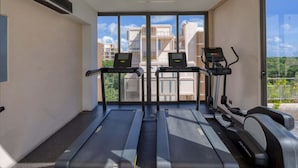 A gym with treadmills and an elliptical machine, large windows, and a view of buildings. - Spacious 2BR with Terrace in The Village (Playa del Carmen)