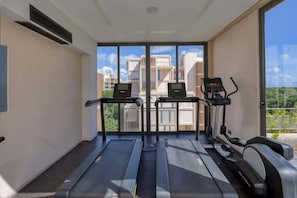 Ein Fitnessraum mit Laufbändern und einem Crosstrainer, großen Fenstern und Blick auf Gebäude.