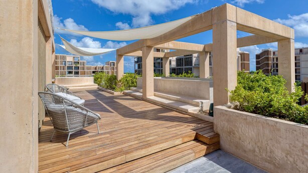 A rooftop terrace with a wooden deck, a metal chair, and a concrete structure with a white canopy. - Spacious 2BR with Terrace in The Village (Playa del Carmen)