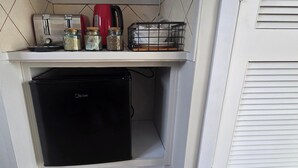 A compact kitchenette with a black refrigerator, a red kettle, and glass jars on a shelf.