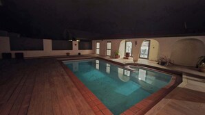 An indoor swimming pool with a wooden floor, a tiled edge, and a view of the outside through a window.
