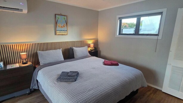 A hotel room with a bed, bedside tables, a window, and a wall-mounted air conditioner.