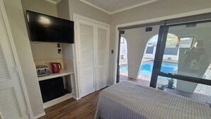 A bedroom with a bed, a television, a coffee maker, and a sliding glass door leading to a pool.