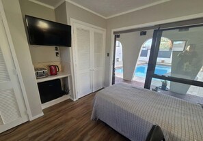 A bedroom with a bed, a television, a coffee maker, and a sliding glass door leading to a pool.