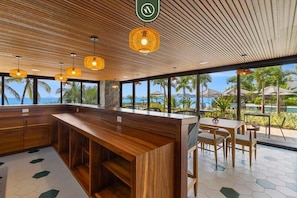 Eine moderne Bar mit Holzmöbeln, großen Fenstern und Meerblick.