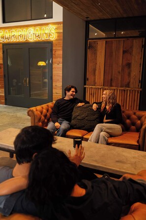 Un rincón acogedor con un sofá de cuero y una mesa, una pared de madera con un letrero de neón y una puerta grande de madera.