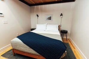 Una cama bien hecha con un cabecero acolchado, una manta azul y dos mesitas de noche con lámparas.