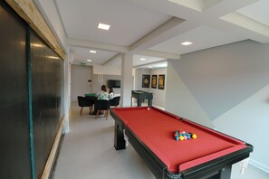 Ein Billardtisch mit Kugeln, ein Kicker und ein Fernseher in einem Raum mit weißer Decke und Wänden.