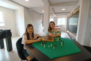 Two individuals seated at a table with a chessboard, in a room with a large window and a blackboard on the wall. - Family Apartment III near Beto Carrero World and the Beach (Penha)