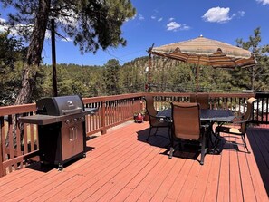 A wooden deck with a barbecue grill, outdoor table and chairs, and a striped umbrella. - Come and enjoy a relaxing getaway in beautiful Ruidoso! Minutes from everything (Ruidoso)