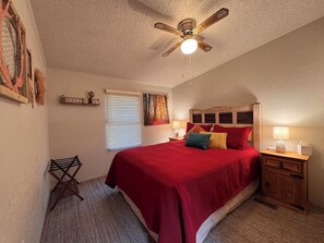 A bedroom with a bed, a ceiling fan, a nightstand, a lamp, a window with blinds, and a wall-mounted shelf. - Come and enjoy a relaxing getaway in beautiful Ruidoso! Minutes from everything (Ruidoso)