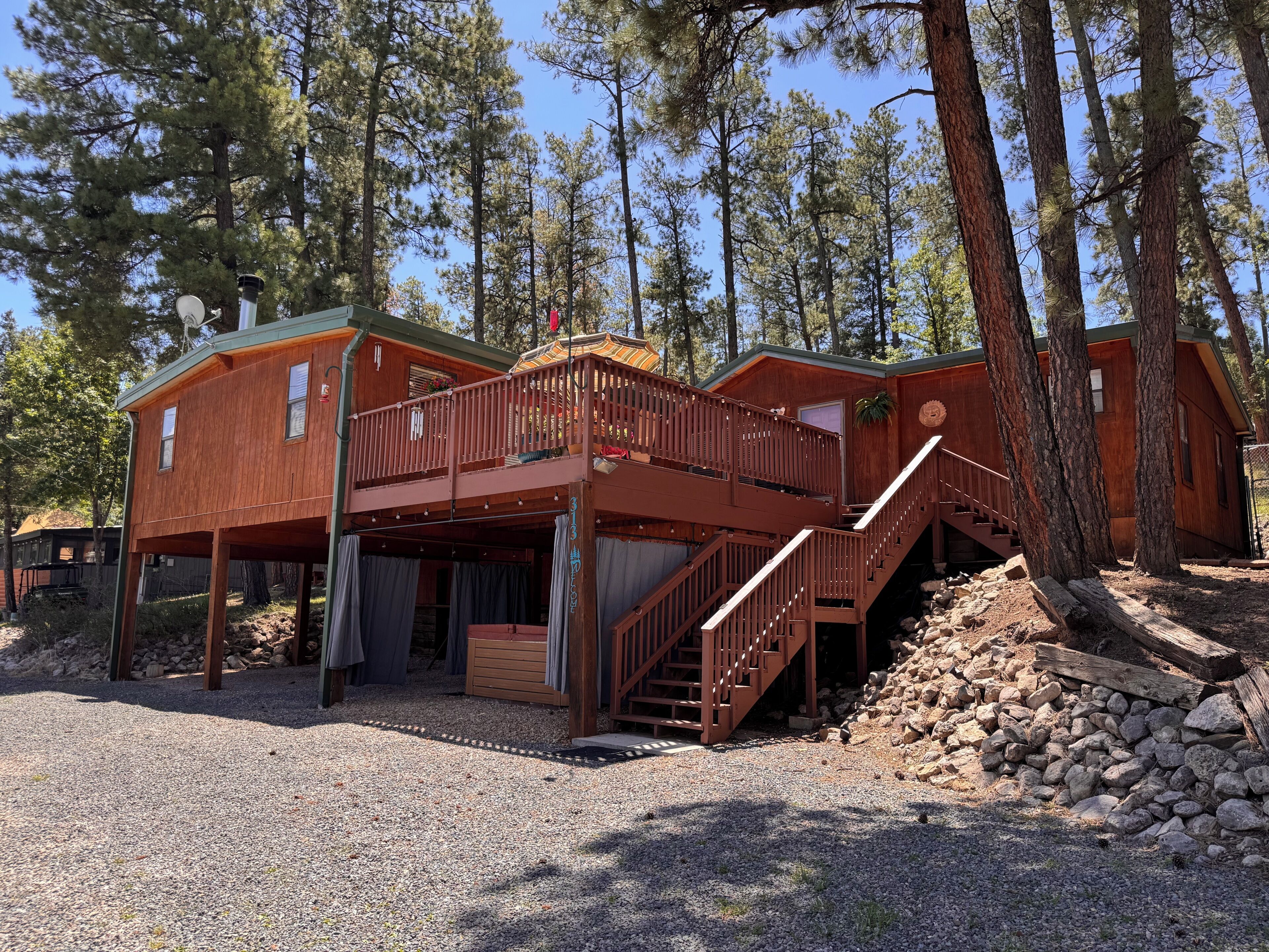 A cabin with a wooden deck, a staircase, and a gravel driveway.