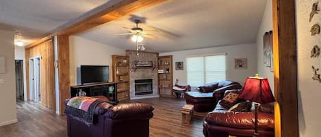 Un salón amplio con chimenea, sofás de cuero, televisión y ventilador de techo.