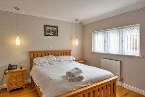 A bedroom with a wooden bed, bedside tables, a telephone, a framed picture on the wall, and a window with blinds.