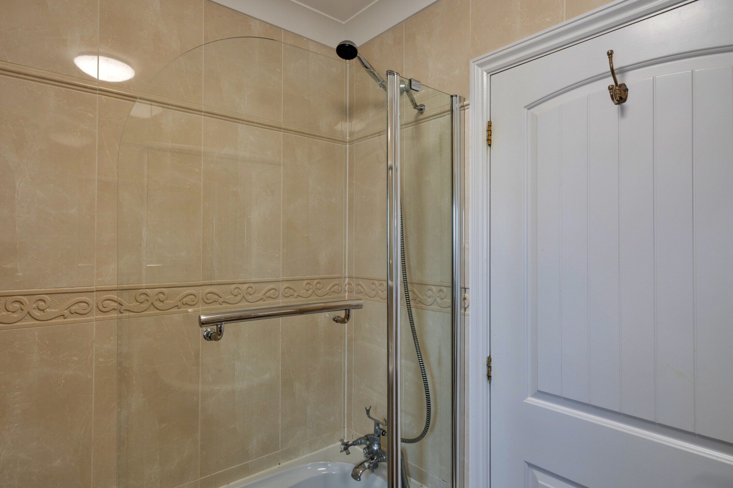 A bathroom with a glass-enclosed shower, a white door, and a decorative tile border.
