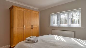 Un dormitorio con un amplio armario de madera, una cama con sábanas blancas y una ventana con persianas.