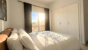 A bedroom with a bed, a wardrobe, and a window with curtains. - El Gouna luxury apartment lagoon and pool view (Hurghada 2)