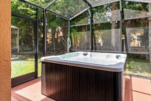 Un bain à remous situé dans un espace clos par des parois de verre, offrant une vue sur un jardin et des arbres.