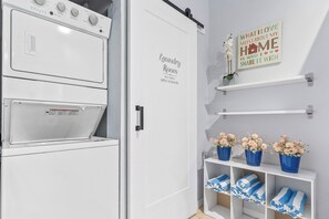 Une laverie avec un espace en libre-service ouvert 24 heures sur 24, une pancarte au-dessus de la porte et des étagères remplies de serviettes et de fleurs.