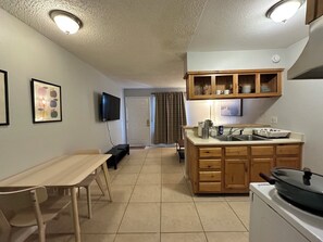 A compact kitchen with a dining area, wooden cabinets, a flat-screen TV, and a tiled floor.