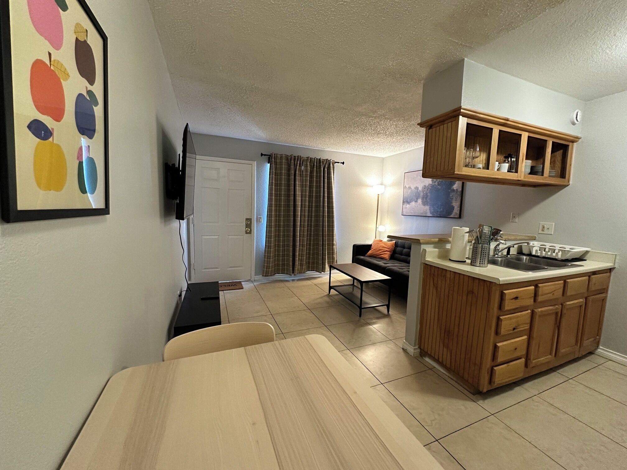A compact kitchen with a dining area, a television mounted on the wall, and a wooden cabinet above the sink.
