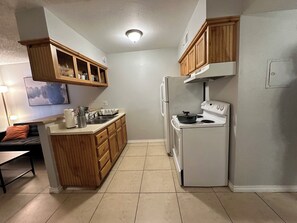 A compact kitchen with wooden cabinets, a refrigerator, a stove, and a dining area with a table and chairs. - Comfortable 1-bedroom with AC Full Kitchen and Laundry in sunny Phoenix (Phoenix)