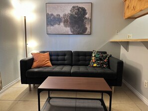 A living room with a sofa, two pillows, a coffee table, a floor lamp, and a painting on the wall.