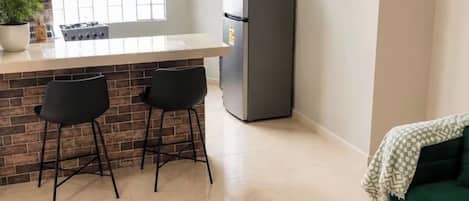 A compact kitchen with a refrigerator, a window, and a bar area with stools.