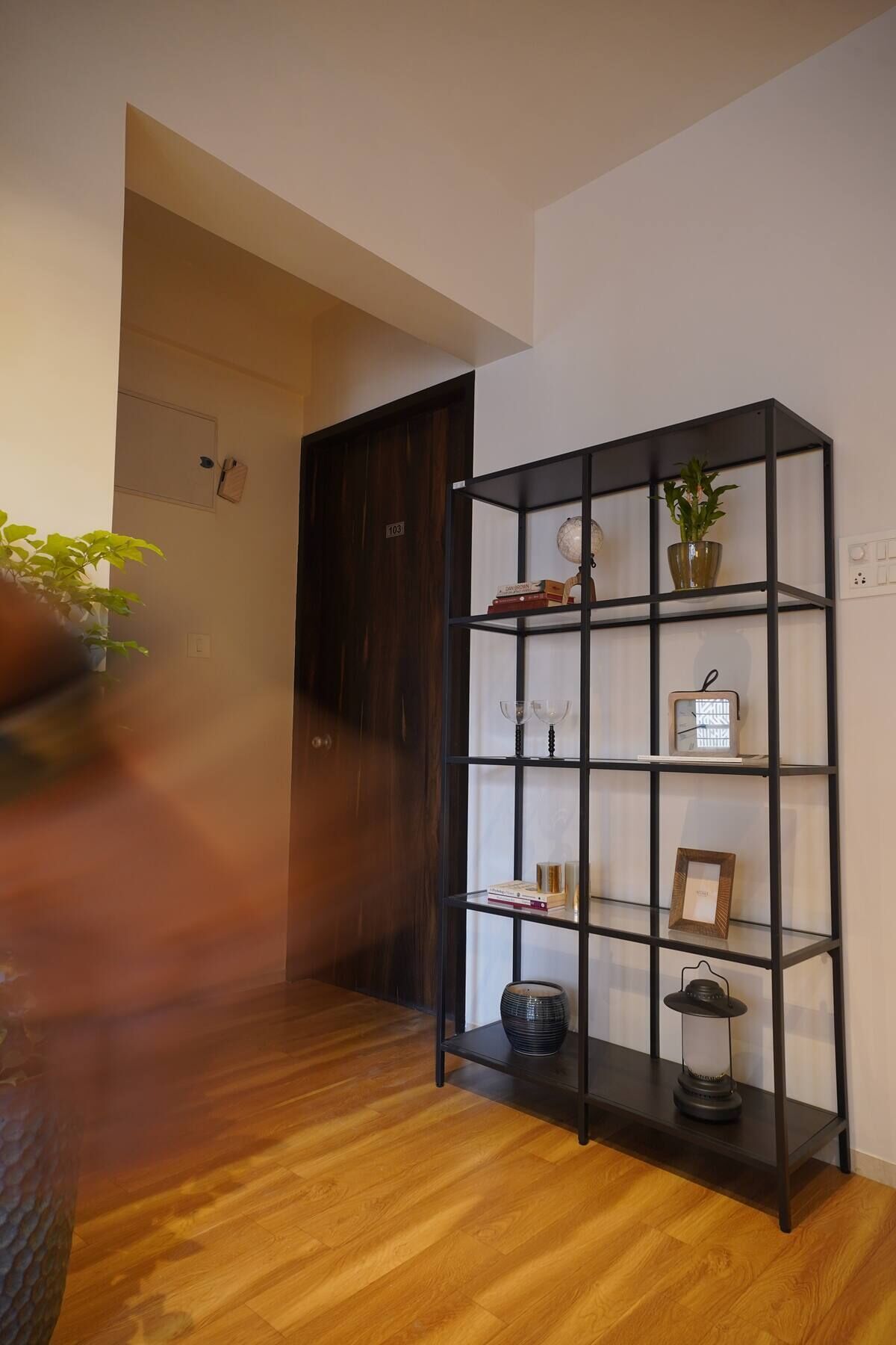 A room with a wooden floor, a black metal bookshelf, and a door.