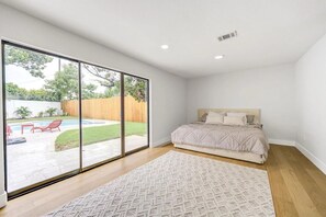 Une chambre dotée d’une grande porte-fenêtre coulissante donnant sur un jardin avec une piscine et du mobilier d’extérieur.