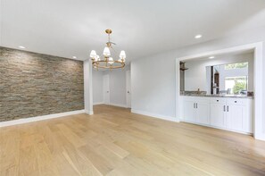 A spacious room with a stone wall, a chandelier, white cabinets, and a wooden floor. - Beautifully Renovated High ceiling spacious 5-bedroom house in Houston with pool (Houston)