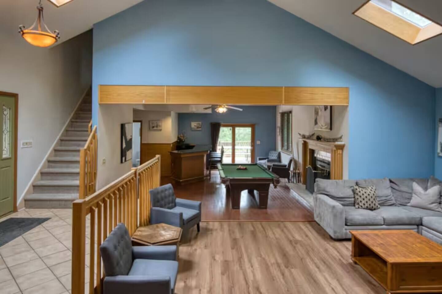 A spacious living area with a pool table, a sofa set, a fireplace, and a staircase leading to another level.