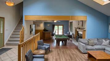 A spacious living area with a pool table, a sofa set, a fireplace, and a staircase leading to another level.