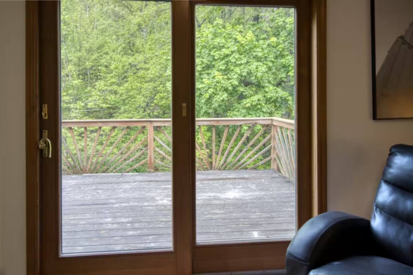 Une pièce dotée d’une porte en bois qui donne sur une terrasse extérieure avec une rambarde en bois, et qui offre une vue sur une zone boisée.