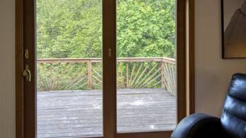 A room with a wooden door leading to an outdoor deck with a wooden railing, overlooking a forested area.