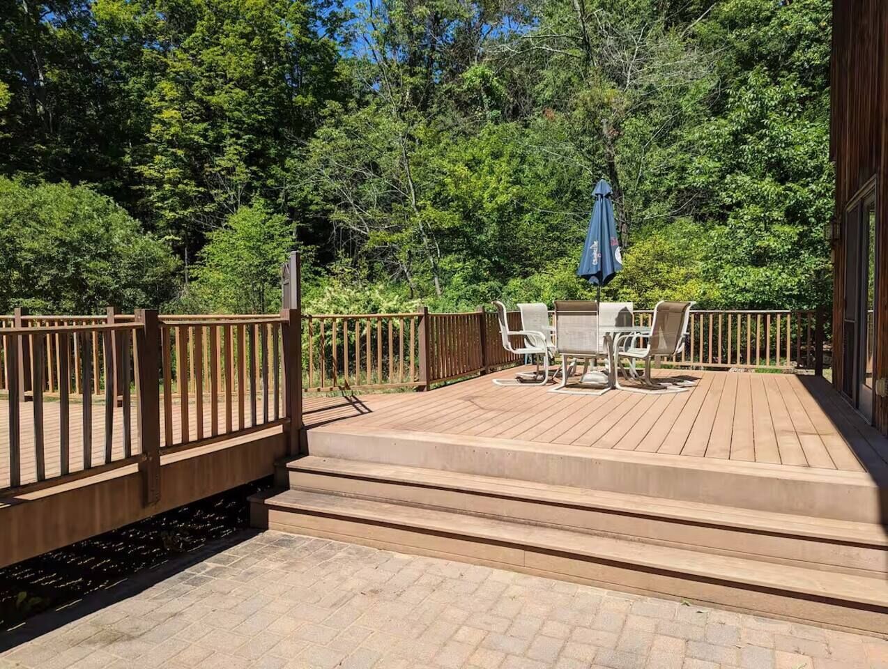 Une terrasse en bois avec une table et des chaises, entourée d’une balustrade en bois et offrant une vue sur une forêt dense.