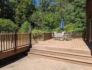 Une terrasse en bois avec une table et des chaises, entourée d’une balustrade en bois et offrant une vue sur une forêt dense.