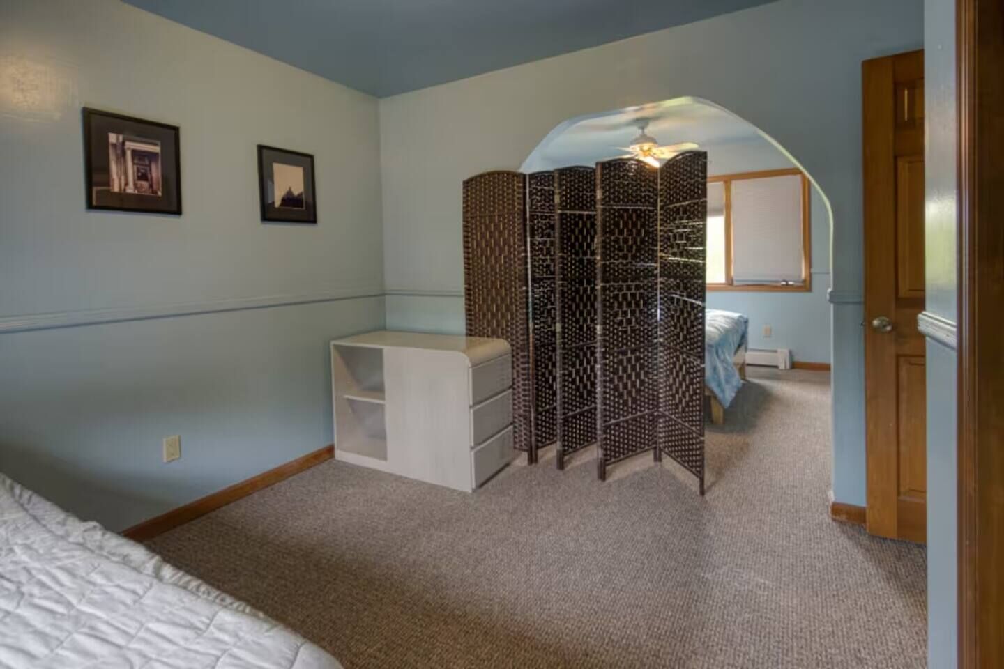 Un dormitorio con cama, cómoda blanca, biombo decorativo y una puerta.