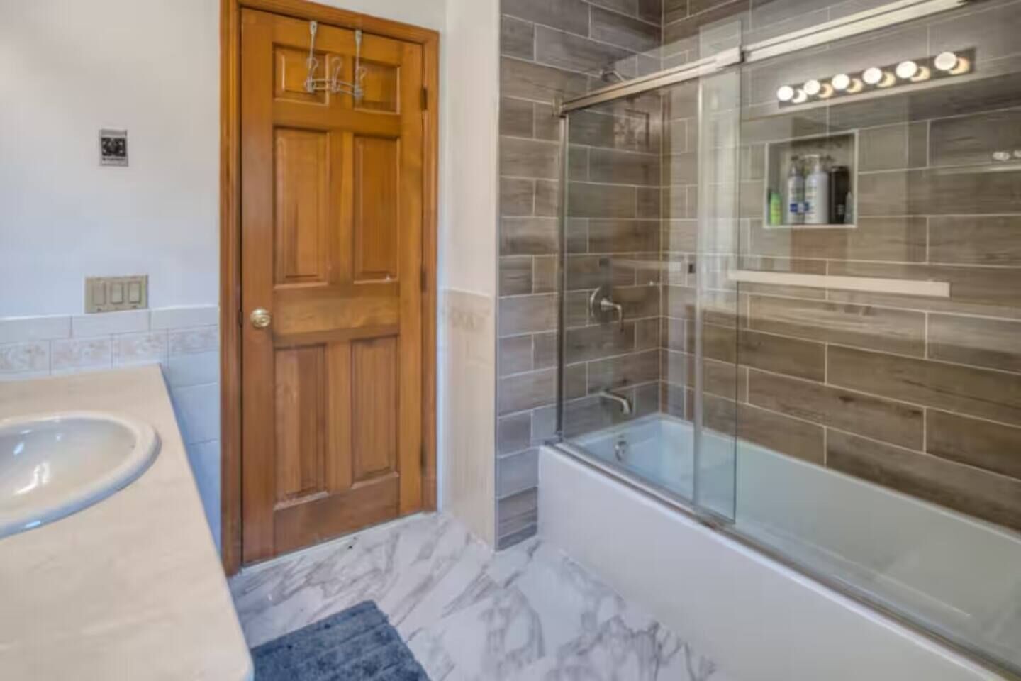 A bathroom with a wooden door, a glass-enclosed shower, and a marble floor.