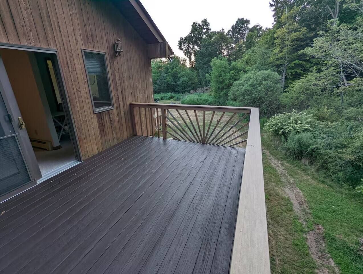 A wooden deck with a railing, leading to a building with a window and a door.