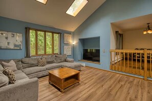 A living room with a sofa, coffee table, and a TV. There are windows and a balcony with a railing. - Secluded 6BR Retreat Near Lake Hopatcong (Roxbury Township)
