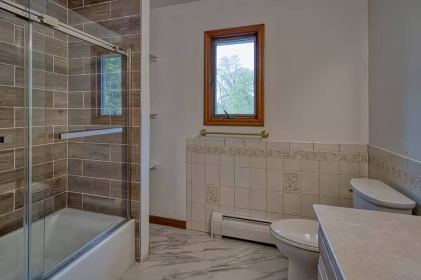 A bathroom with a glass shower enclosure, a toilet, and a window.